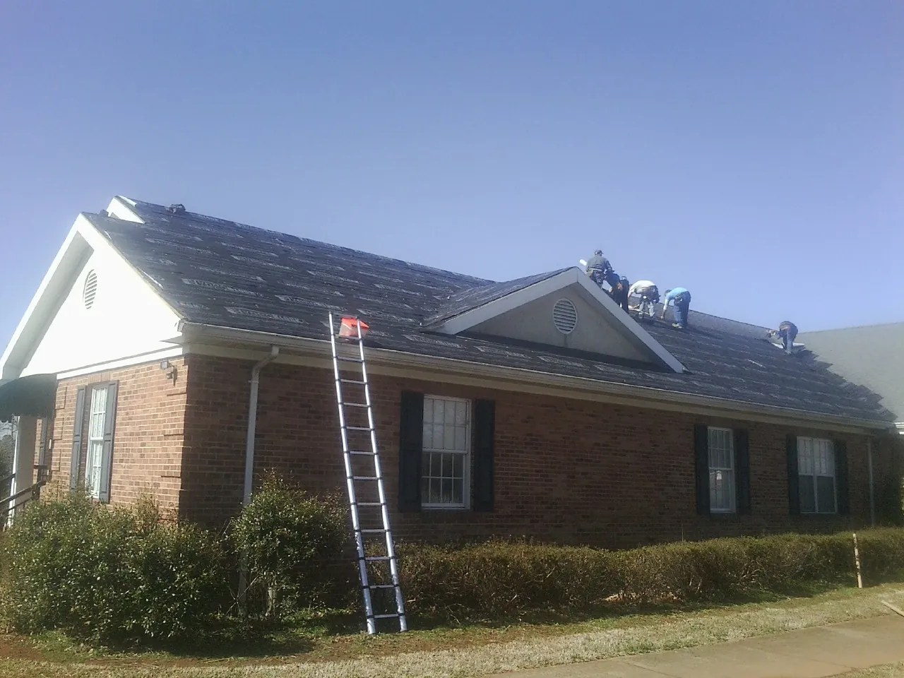 Crew tearing shingles off a brick ranch roof with a ladder set — Emergency Roof Repair work by our crew in Cannon Falls