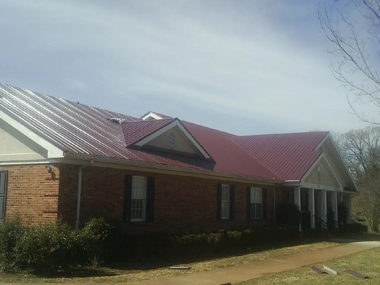Red metal roof with gabled entries on a long brick building, from a Hail Damage Roof Repair job in Cannon Falls