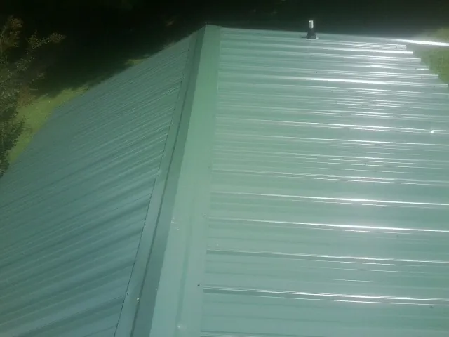 New green metal panels meeting at the ridge of a roof — Flat Roof Repair work by our crew in Cannon Falls