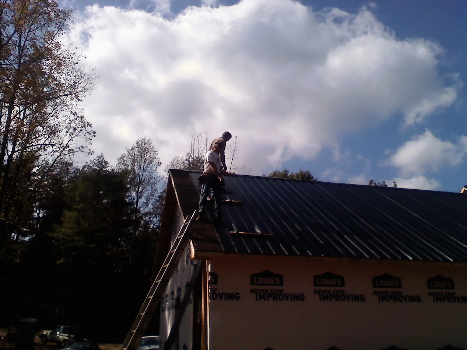 Roofer fastening dark metal panels high against a cloudy sky, from a Roof Inspection job in Cannon Falls