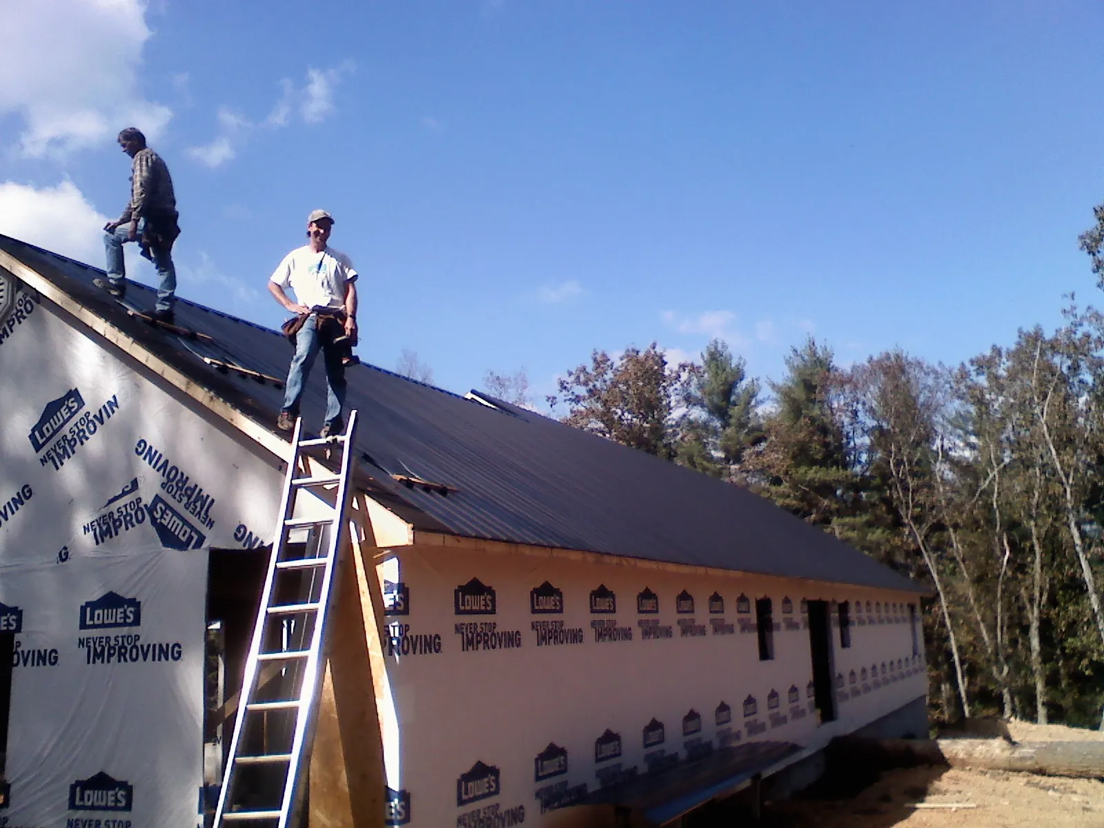 Two roofers standing on a long dark metal roof over a wrapped building in Cannon Falls