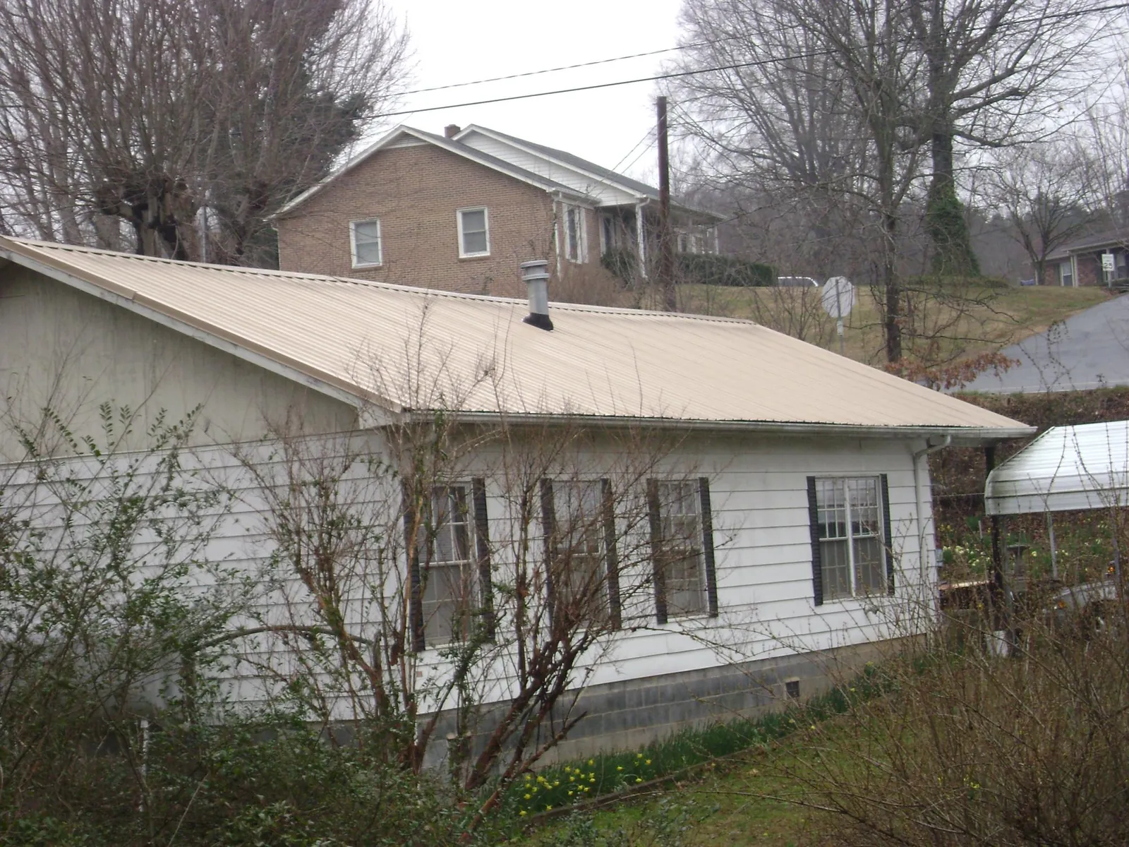 Tan metal roof on a white sided house set into a hillside — Commercial Roofing by Roofing Brothers in Cannon Falls