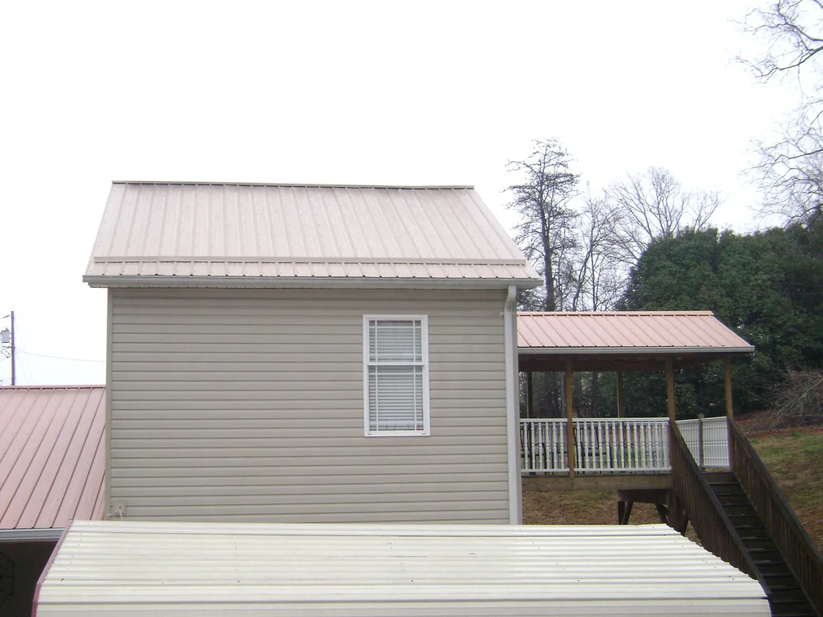 Tan metal roofs on a two story addition and attached porch, from a Roof Replacement job in Cannon Falls